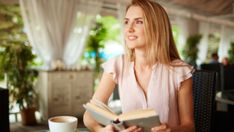 a woman sitting at a table with a book in her hand and a cup of coffee