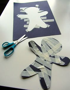 paper cut out of the shape of a person and scissors on top of a table