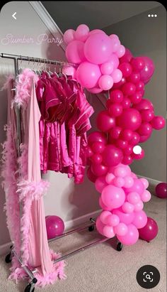 some pink balloons are hanging from a rack in a room with clothes and other items