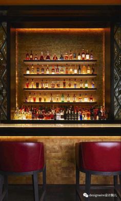 two red chairs sitting in front of a bar with bottles on the wall behind it