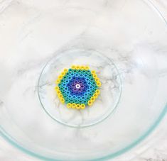 a beaded object in a glass bowl on a marble countertop, with water droplets around it