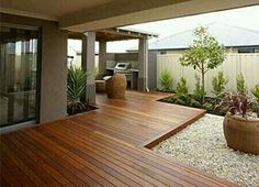 a wooden deck in the middle of a yard with plants and rocks on it, next to an outdoor kitchen