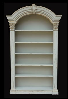 an old white bookcase with ornate carvings on the top and bottom shelves, against a black background