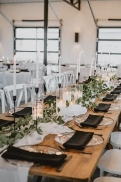 the table is set with black and white place settings, candles, and greenery