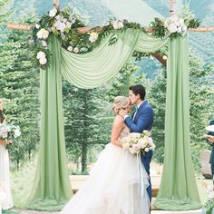 a bride and groom standing under an outdoor wedding ceremony arch with greenery draped over it