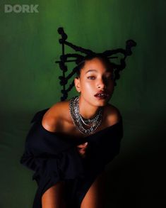 a woman with dreadlocks on her head is posing for a photo in front of a green background