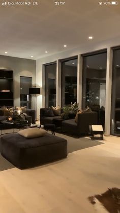 a living room filled with lots of furniture next to tall glass windows in front of them