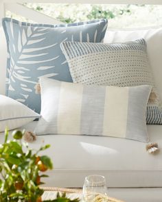 a white couch with blue and white pillows on it's back, next to a glass of wine