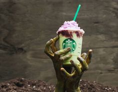 a hand holding up a starbucks drink in front of a pile of dirt with one hand on the cup