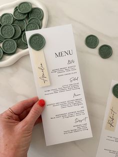 a person holding up a menu card next to some green wax seals on a table