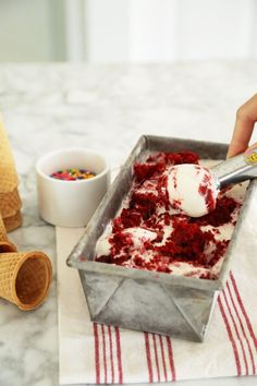 a person scooping ice cream into a pan on a table next to some cones