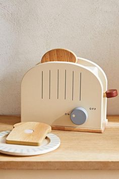 a toaster sitting on top of a wooden counter next to a plate with a slice of bread