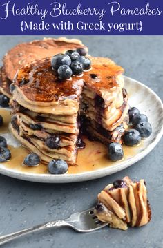 a stack of pancakes with blueberries and syrup on a plate next to a fork