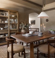 a dining room table and chairs in front of a book shelf with plates on it