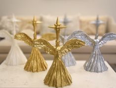 three gold and silver angel figurines sitting on top of a white coffee table