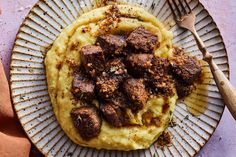 a white plate topped with meat and grits on top of a purple tablecloth