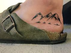 a tattoo on the foot of a woman with mountains in the background and birds flying around