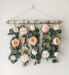 an arrangement of flowers hanging on a wall next to a wooden stick with leaves and branches