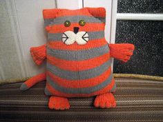 an orange and gray knitted cat pillow sitting on top of a couch next to a window