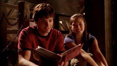 a man and woman sitting next to each other on the floor looking at a book