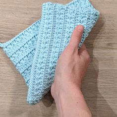 a hand holding a blue crochet dishcloth on top of a wooden table