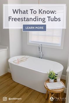 a white bath tub sitting under a window next to a wooden table with a potted plant