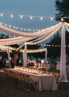 a long table with candles and lights on it is set up for an outdoor dinner