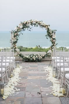 an outdoor ceremony setup with white flowers and petals on the aisle, overlooking the ocean