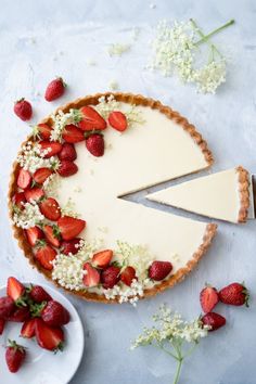 a cheesecake topped with strawberries on a white plate next to flowers and a knife