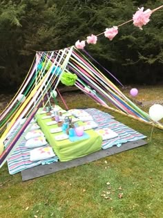 a picnic table set up in the grass with balloons and streamers hanging from it