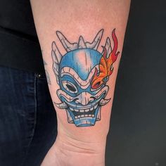 a tattoo on the arm of a person with a blue mask and flames in it