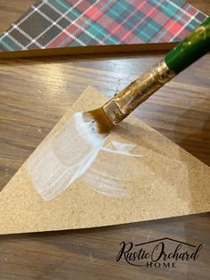 a painting brush is being used to paint the top of a piece of paper on a wooden table