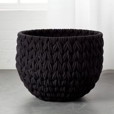 a large black basket sitting on top of a cement floor next to a white wall