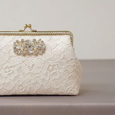 "An exquisite rhinestone bridal clutch for all those wedding day essentials. This stunning clutch features ivory french alencon lace atop ivory silk, secured closure with a brass purse frame and embellished with a blink of rhinestone along on both side of the purse frame. Comes with removable chain strap. This clutch purse is suitable for weddings, both formal and informal party and big enough to carry all your most needed essentials. Dimensions: Frame width : 7\" (measured across the opening) H Classic White Bridal Accessories For Formal Occasion, Elegant Embellished Lace Bridal Accessories, Elegant Lace Bridal Accessories For Ceremony, Elegant Lace Bridal Accessories For Formal Occasions, Elegant White Bridal Accessories For Wedding, Formal Lace Bridal Accessories, Elegant Bridal Accessories With Lace Work For Ceremony, Cream Bridal Accessories For Mother Of The Bride, Elegant Lace Bridal Accessories For Evening