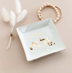 a white square plate with the words future mrs on it next to a feather and beaded bracelet