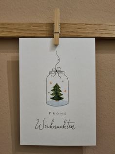 a christmas card hanging from a clothes line with a tree in a jar on it