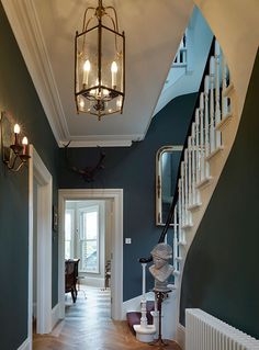 a hallway with blue walls and wooden flooring next to a white stair case in front of a window