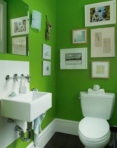 a small bathroom with green walls and pictures on the wall above the toilet, along with a white commode