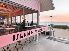 people sitting at tables in front of a pink restaurant with the ocean in the background