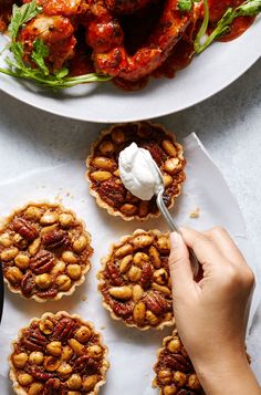 a person is spreading cream on top of small pies that are topped with nuts