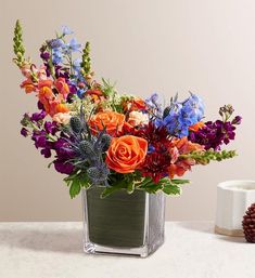 a vase filled with lots of colorful flowers on top of a white table next to a pine cone