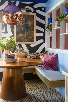 a room with a table, couch and potted plants in front of a painting on the wall