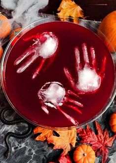 a glass bowl filled with red liquid and two hand prints on top of it, surrounded by fall leaves