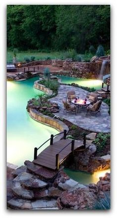 an outdoor swimming pool surrounded by rocks and water features a bridge that leads to a waterfall