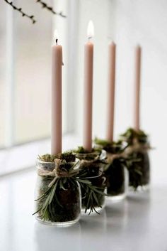 three candles are sitting in small jars with moss and pine cones on the top one