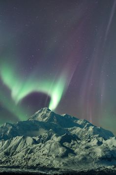 an aurora bore is seen above the snow covered mountains in this photo, with green and purple lights