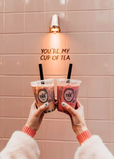 two people holding up cups in front of a wall with the words you're my cup of tea on it