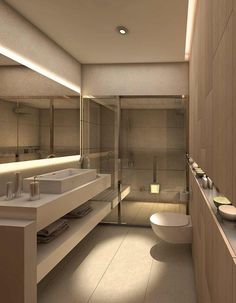 a modern bathroom with two sinks, toilet and shower in the background is illuminated by recessed lighting