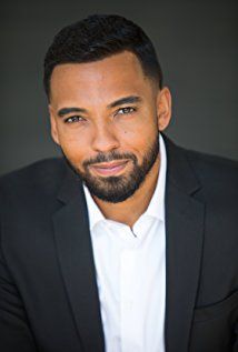 a close up of a person in a suit and tie with a beard smiling at the camera