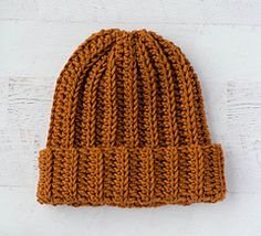 an orange knitted beanie sitting on top of a white wall